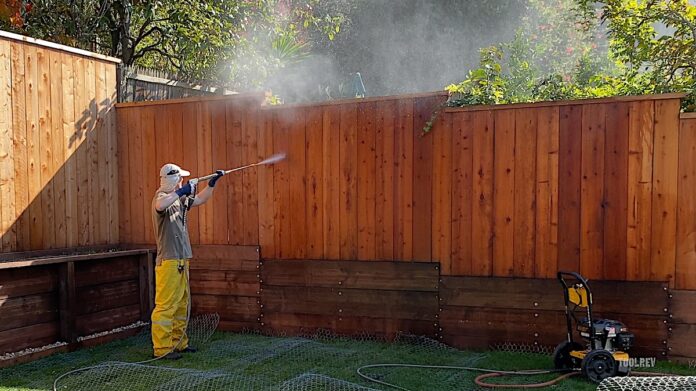 Man pressure washing a fence.